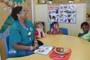 Instructor Cherri Strickland sits with Alaina Campos, Krissa Clavell and Renee Smith at Watters CDC #2 Tuesday. Strickland used Creative Curriculum techniques to help teach the children about the difference between big and small, using the items on the tray pictured to provide visual examples.